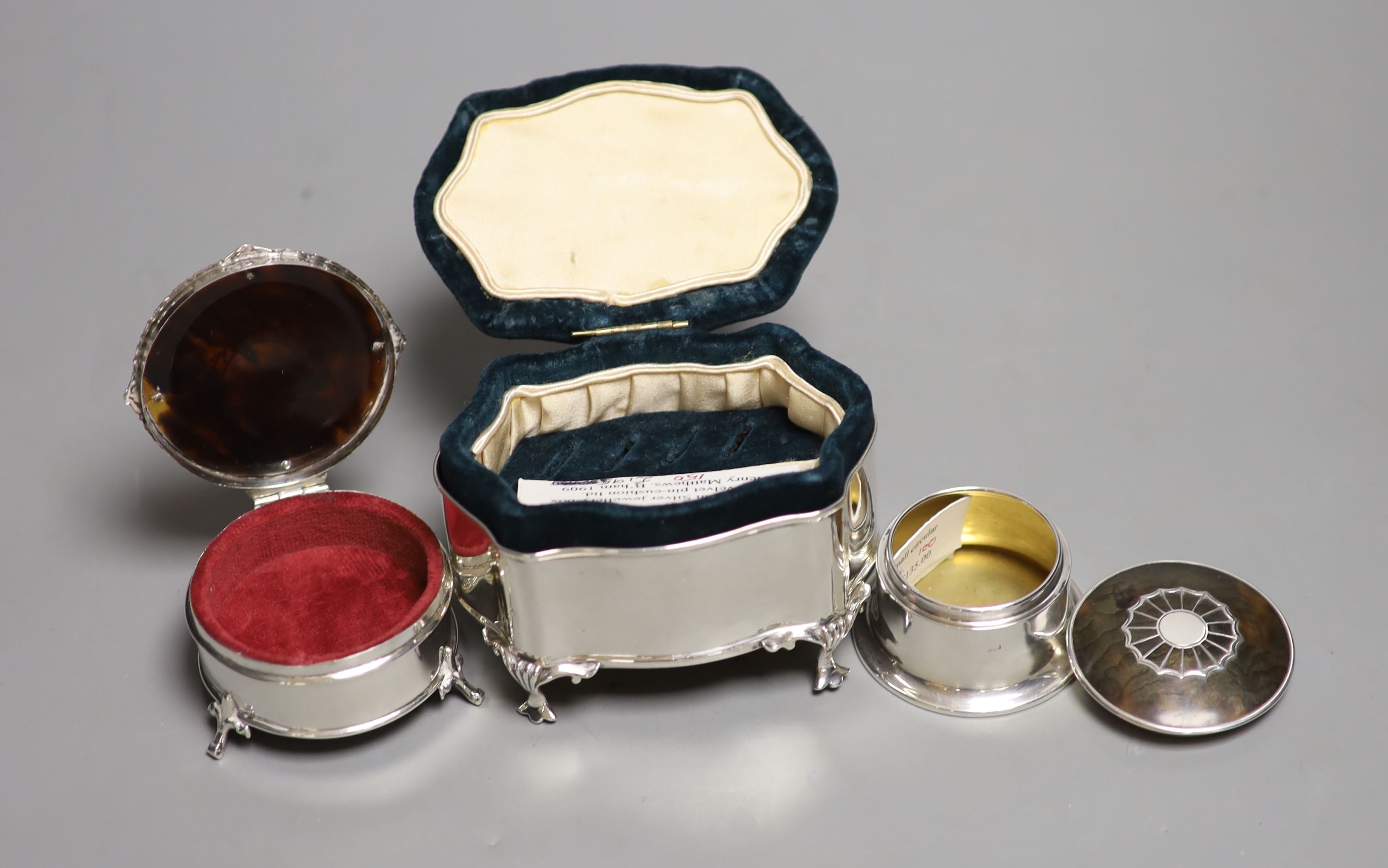 An Edwardian silver mounted pin cushion, Birmingham, 1909, length 10cm and two George V silver and tortoiseshell pique circular trinket boxes.